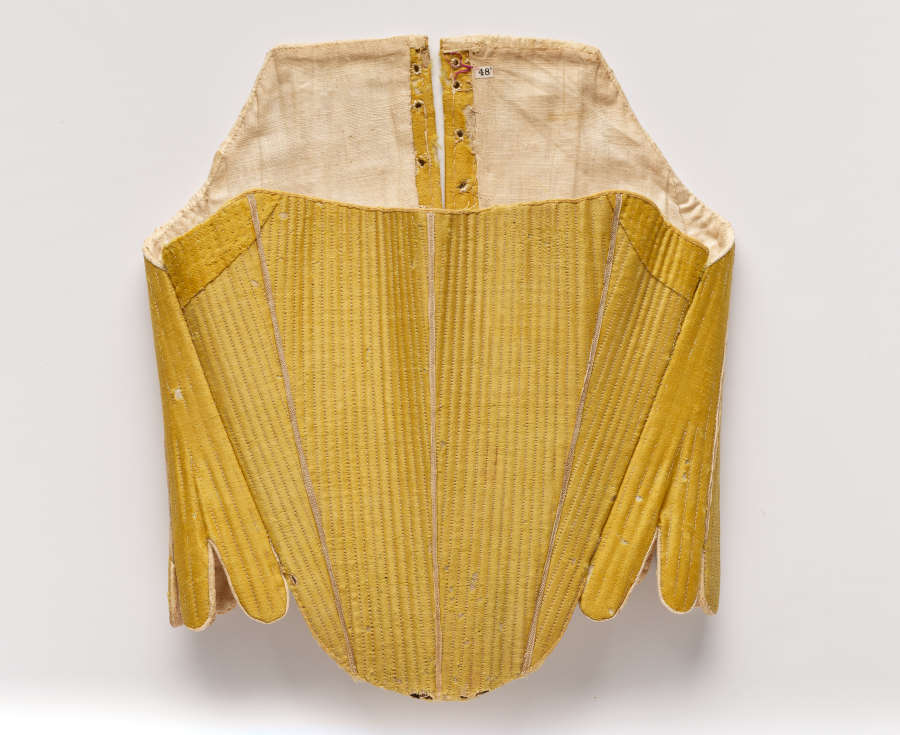  Photo of the back of a stitched gold-colored garment. Constructed of many panels, it is scalloped at the bottom.