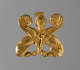 Gold ornament of two sphinx bodies facing one another. At their intersection is the gold crowned head of a woman, framed by two symmetrically arranged engraved wings.