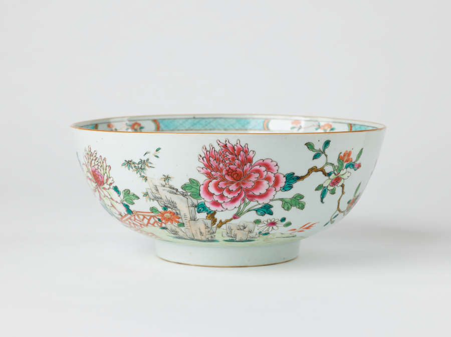 A white punch bowl with a short foot and teal, green, pink, and red floral decorations along the body and inside of the vessel.