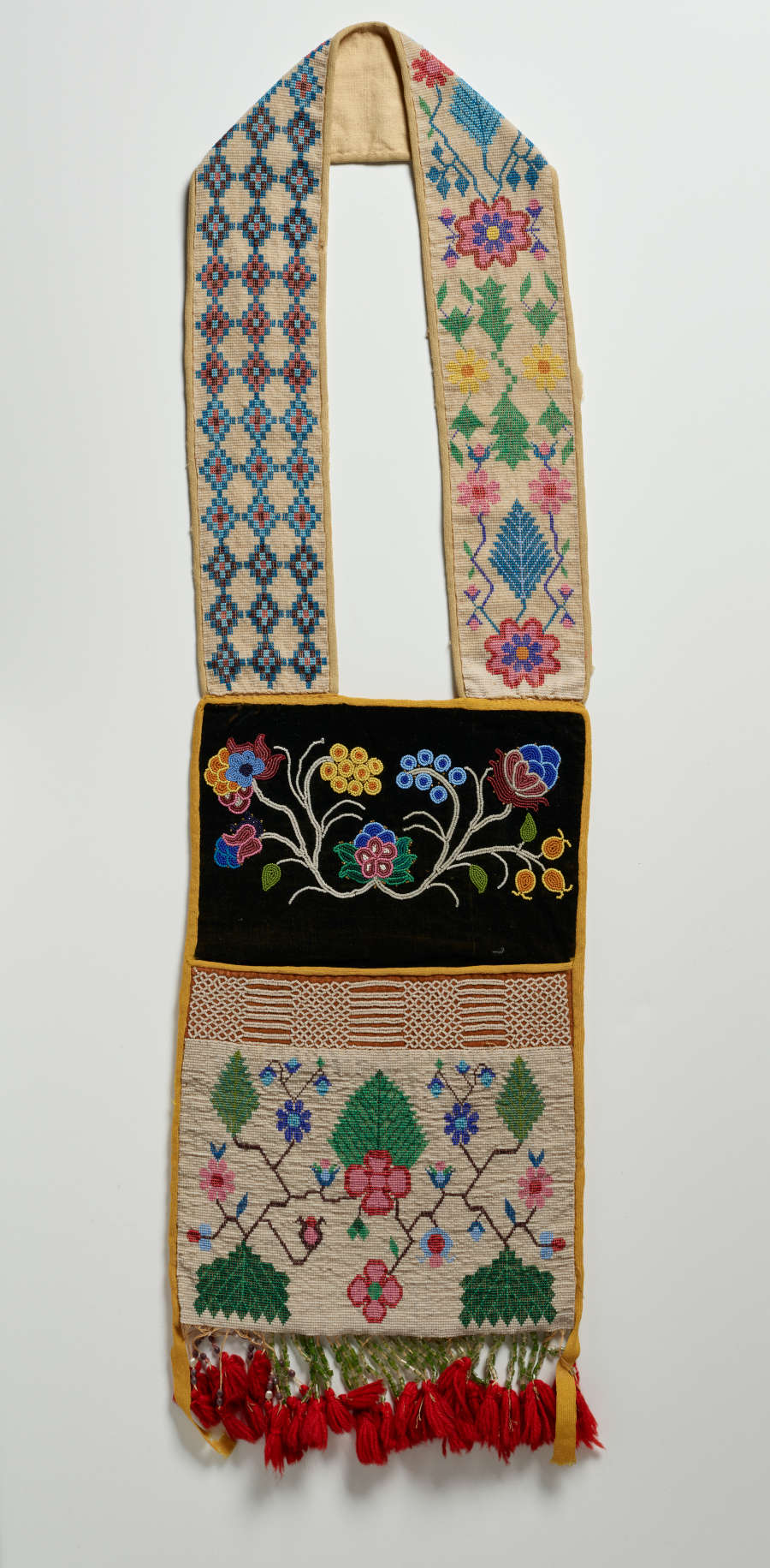 Beige embroidered bag with red tassels lining the bottom featuring a muted geometric diamond pattern on the sash and various intricate and colorful floral patterns adorning the body.