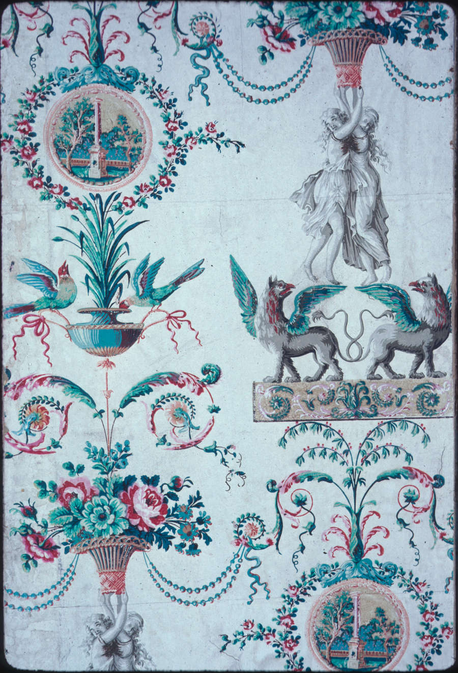 Blue-toned wallpaper featuring small, circular landscape paintings surrounded by floral wreaths with stone figures holding floral bouquets and standing on mythical winged creatures.