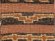 Detail of the patterning on a black and terracotta striped woven bag. On the black stripes, orange geometric patterns are framed by cream threads.