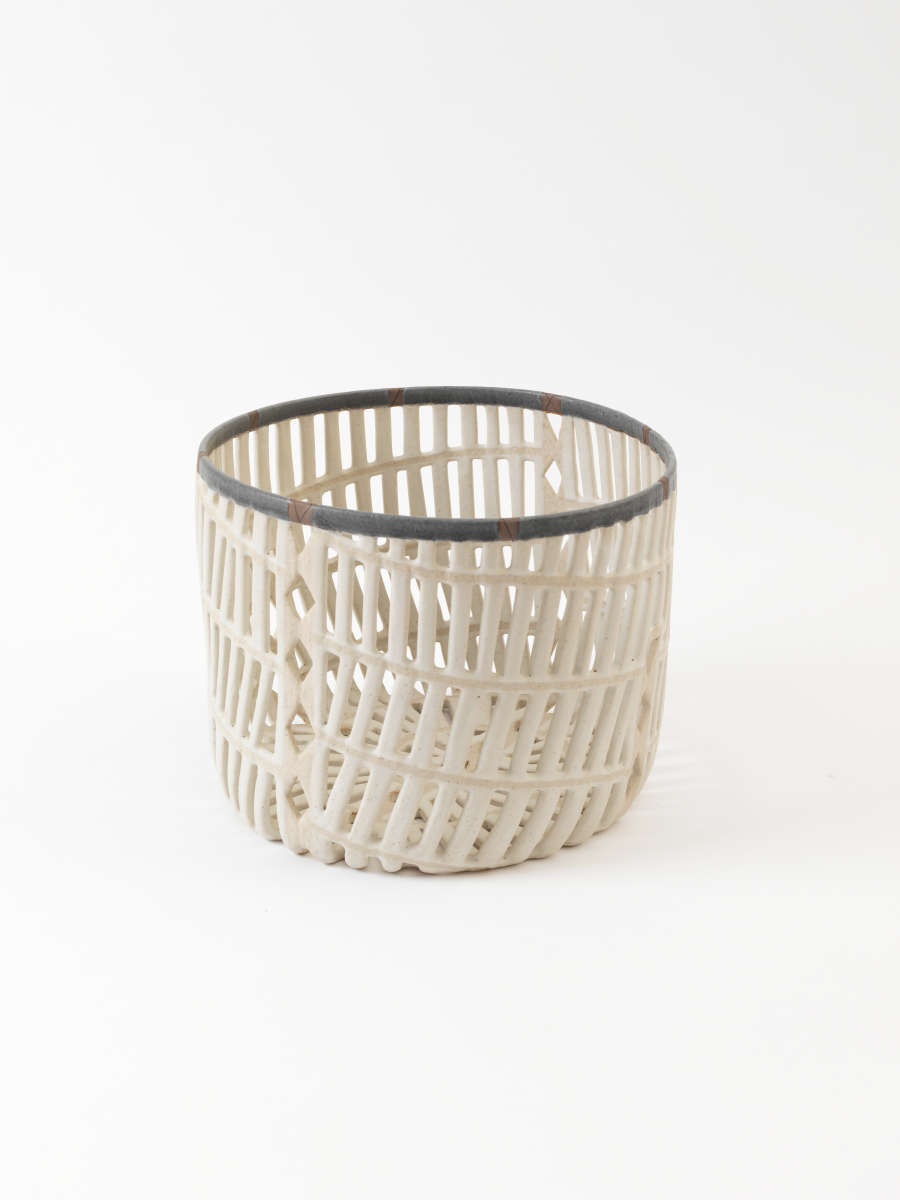 Delicate white basket-like cup constructed of intersecting lattices forming an airy woven grid with narrow open slats and a dark gray edge around the opening.