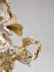 A cherub with small gold, feathered wings holds the end of a leafy garland, perched upon a larger silver-robed figure with butterfly-like gold wings. 