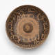 Top-view of the worn brown ceramic bowl with black patterning of animals walking along its rim surrounded by floral motifs. A small dome rises from the bowl's wide, unpainted center.