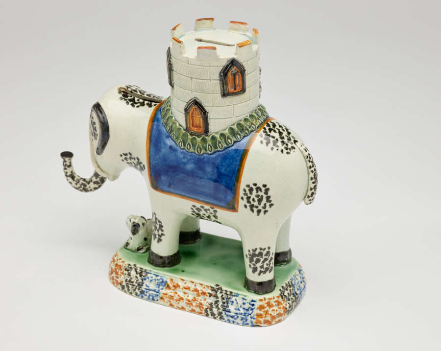  A sculpture in the shape of an elephant with a castle on its back. The decorations are white, blue, green, and yellow.
