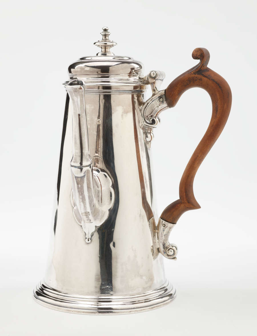 A silver chocolate pot with a spout, hinged lid, and fruitwood handle that is 90 degrees from the spout.
