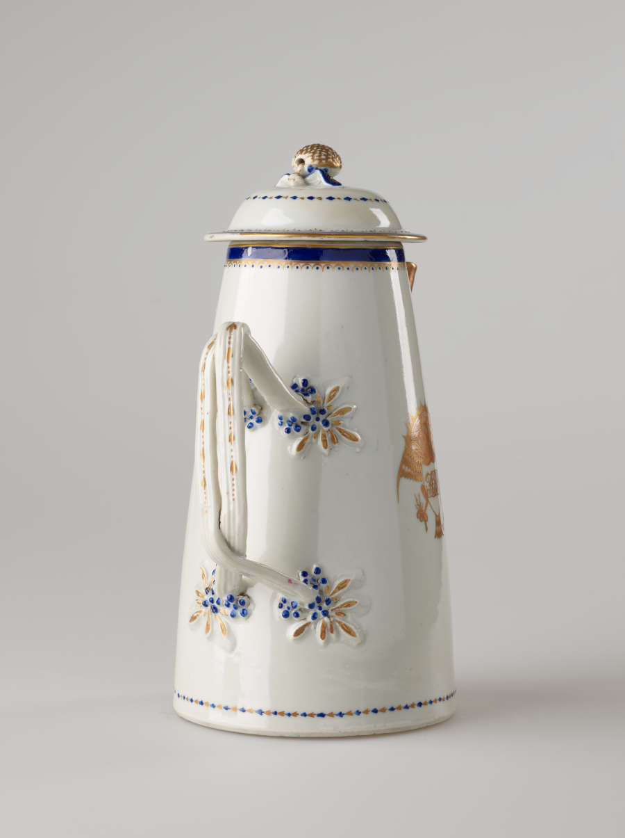 A white, blue and gilded teapot with a long straight spout, a handle, and lid. The central decoration depicts a heraldry bird with a shield and objects in its talons.
