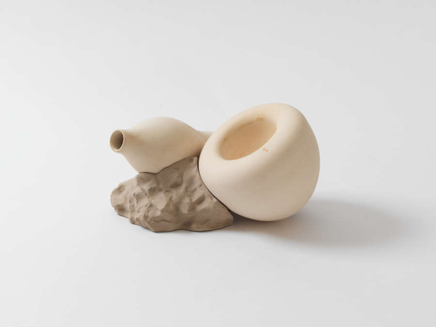 A sculptural piece with two cream-colored bulbous forms resting on a stone-like base.