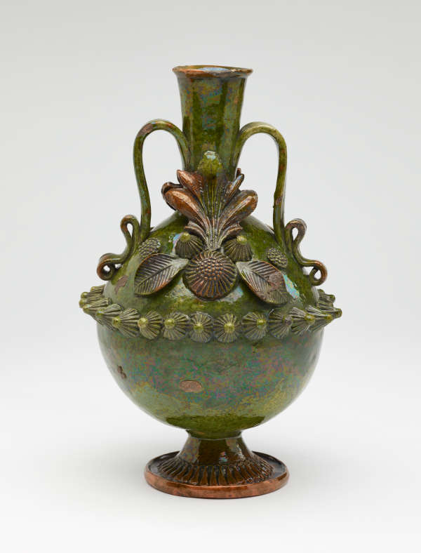 A dark green jug with sculpted decorations, symmetrical decorative handles, and a foot.