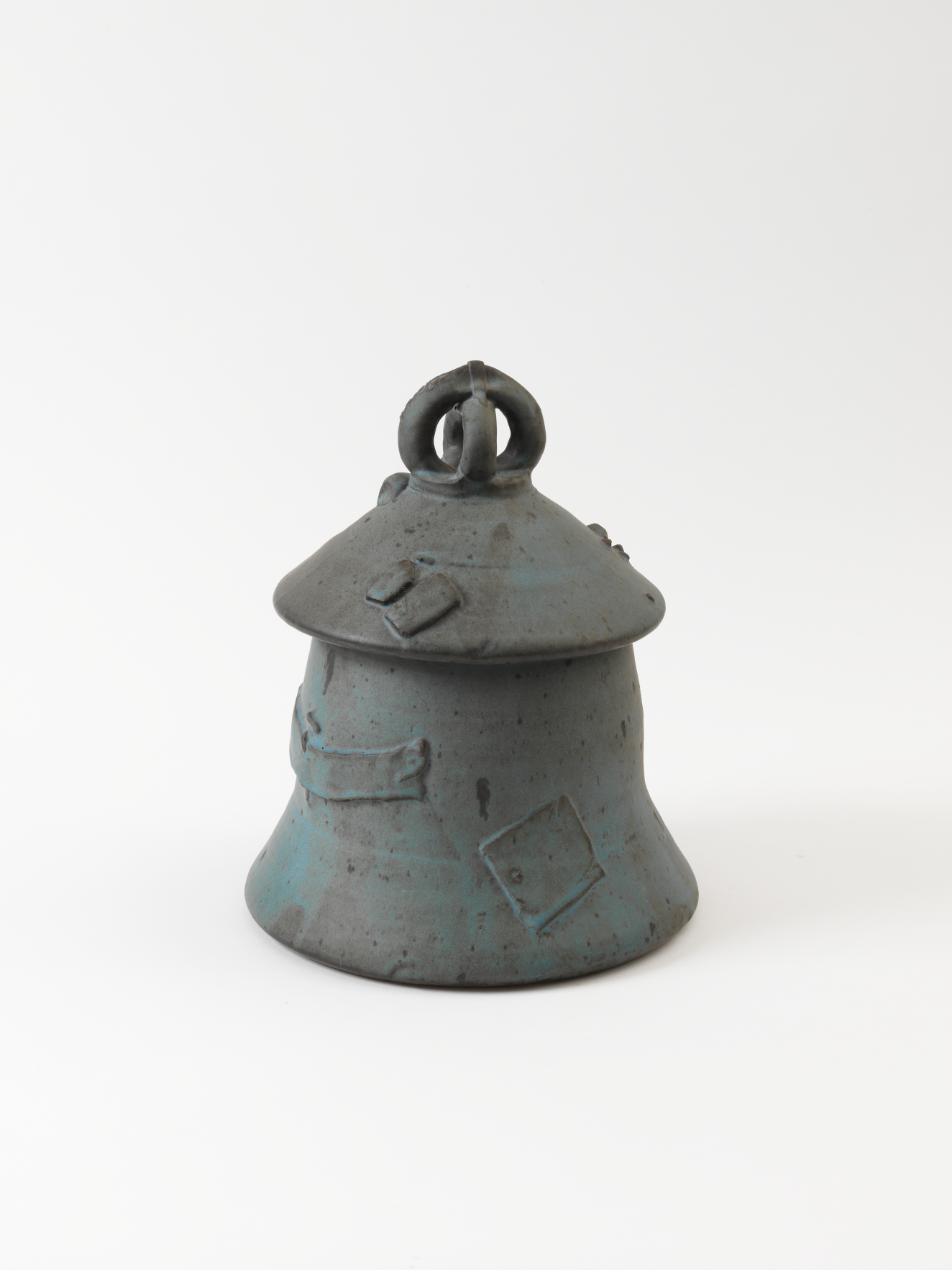 Bell-shaped ceramic jar in blue-gray tones, featuring a domed lid with a looped handle and embossed rectangular patches of varying size and shape scattered across the surface randomly.