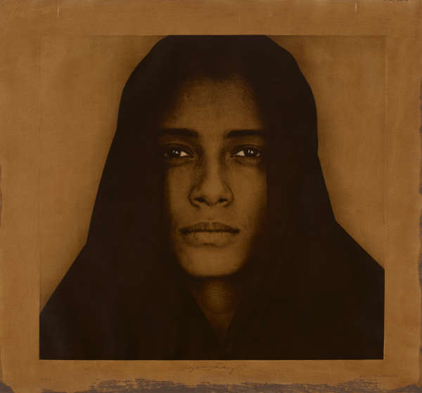 A warm, brown toned portrait of a person draped in a dark hood with a solemn expression.