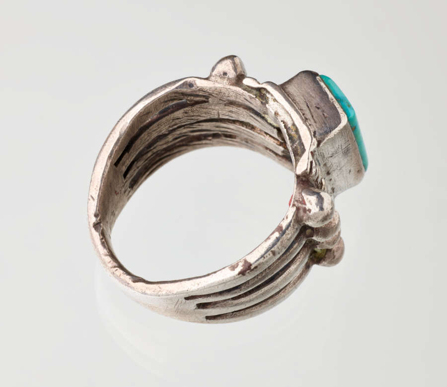 Top-view of a silver metal ring with a turquoise stone-setting. Visible are the inner grooves flowing across the band’s interior and towards the stone. 