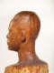 Close-up, three quarter back view of a textured, but glossy, wooden-carved bust depicting a male figure. The base and neck is blurred, highlighting the details in the head.