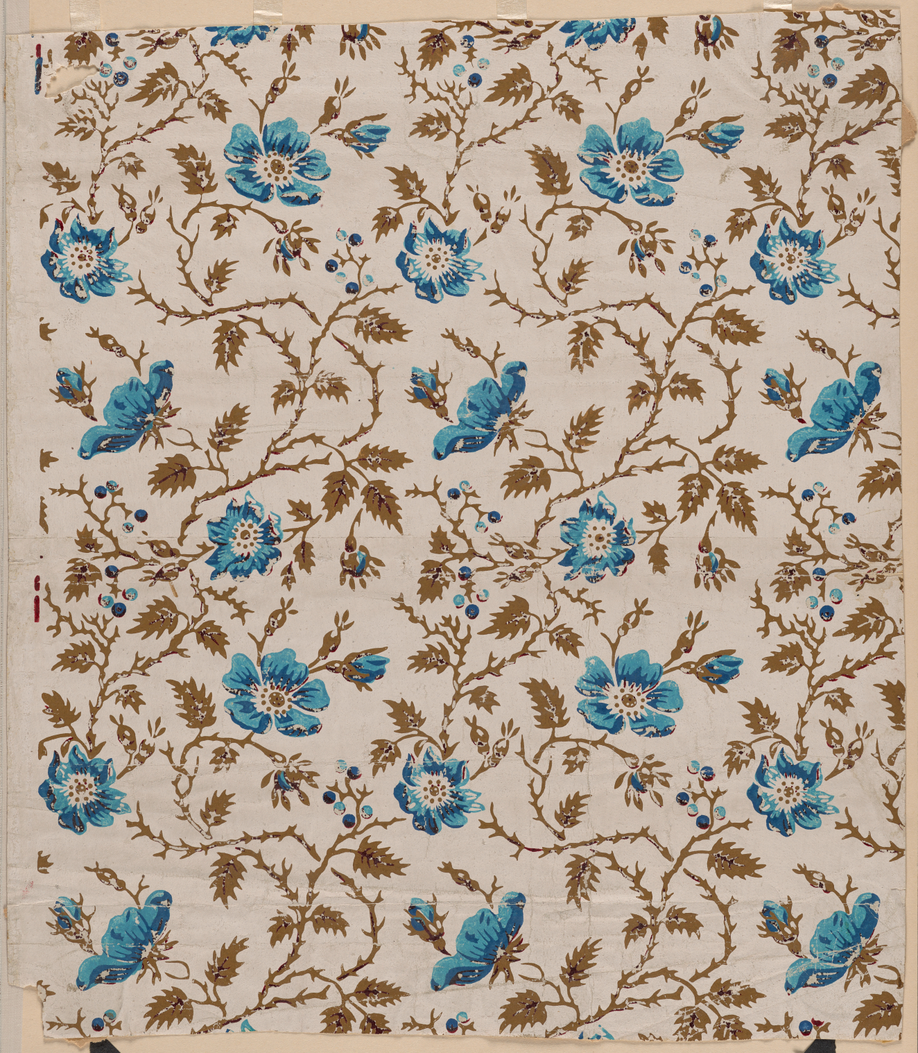 Tan, aged wallpaper of winding olive brown thorny branches and leaves with blue flowers and tiny light and dark blue dots throughout.