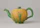 A teapot in the shape of a pineapple. Handle, foot, lid, and spout are green.