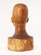 Back view of a glossy wooden bust depicting the head of a  male figure. The wood is cracked while retaining smooth contours, it also features carving marks and color variation.