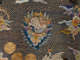 An embroidered circular emblem featuring a mythical creature, surrounded by multicolored swirling clouds and golden medallions, set on gold mesh. 