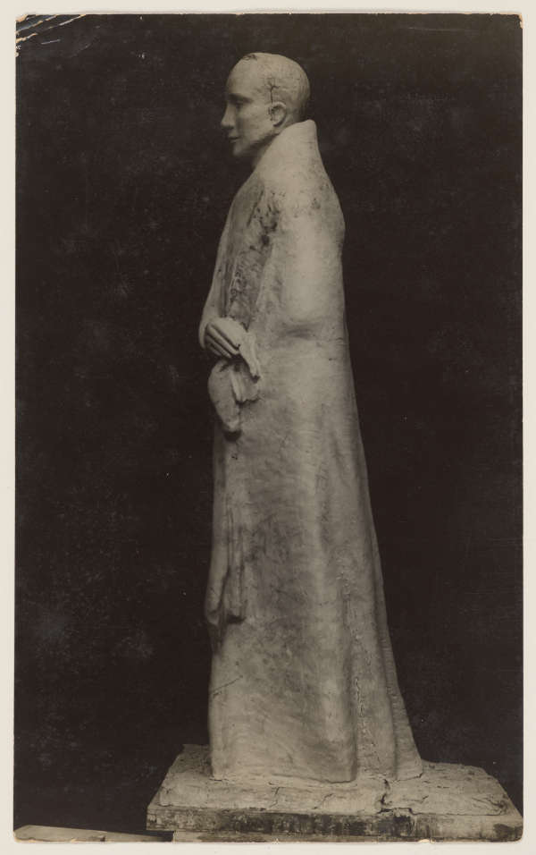 Photograph depicting a sculpture of a robed male presenting figure in profile, showing textured details, against a dark background. The face looks serene and body language demonstrates a calm demeanor.