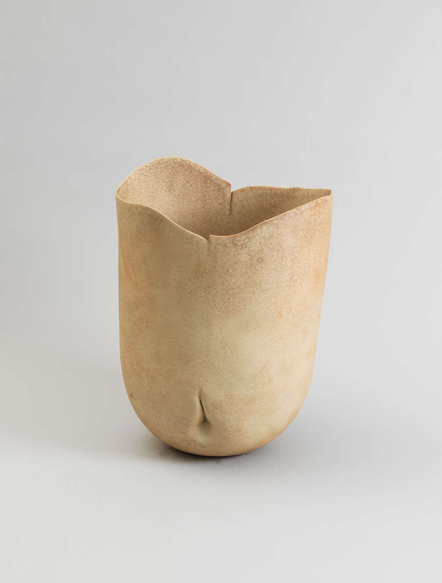 Cream-colored ceramic vessel with soft organic curves and an uneven rim resembling soft folds, marked by a single delicate dimple along the rounded base that suggests an abstracted human torso.