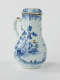 A white chocolate pot with blue decorations depicting floral and architectural elements.