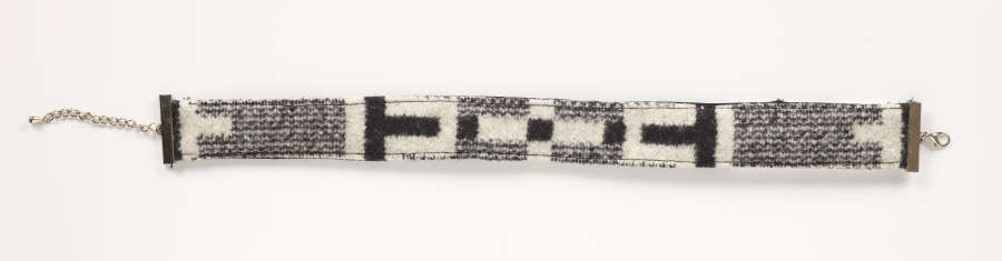 Gray tweed choker with black and white geometric patterning against a white background. A silver metal clasp is on the right side with silver attachment hooks on the left. 