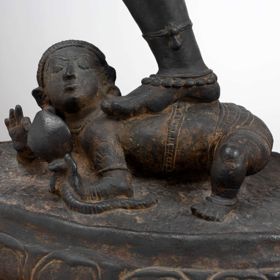 Detail of the sculpture’s bottom showing the figure’s foot stepping on another figure laying stomach down, head and one hand raised. The bottom figure’s body features sculpted patterning.