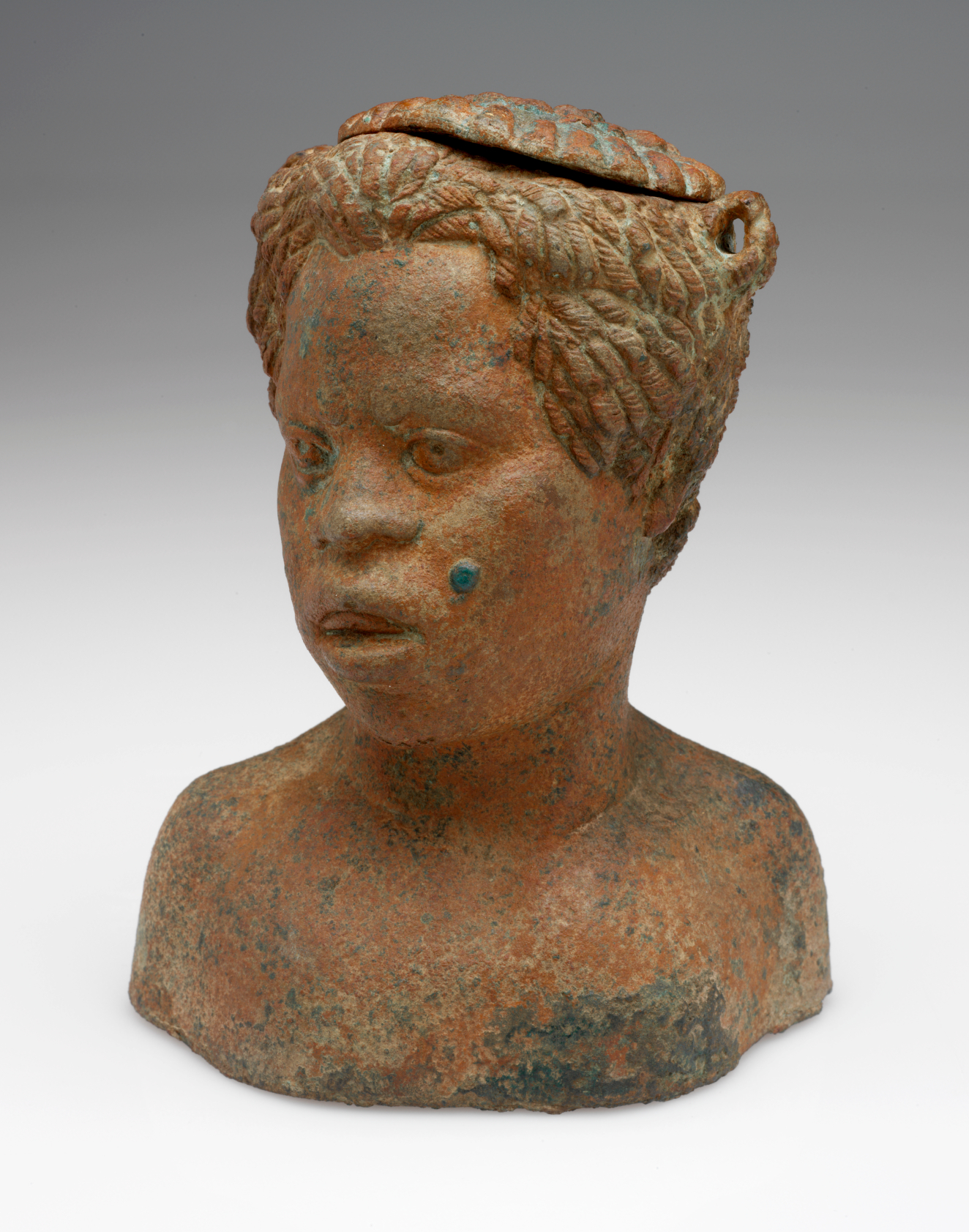 A bronze colored bust of a person with textured hair, detailed facial features, and a cracked opening at the top of the head, looking to the left. 