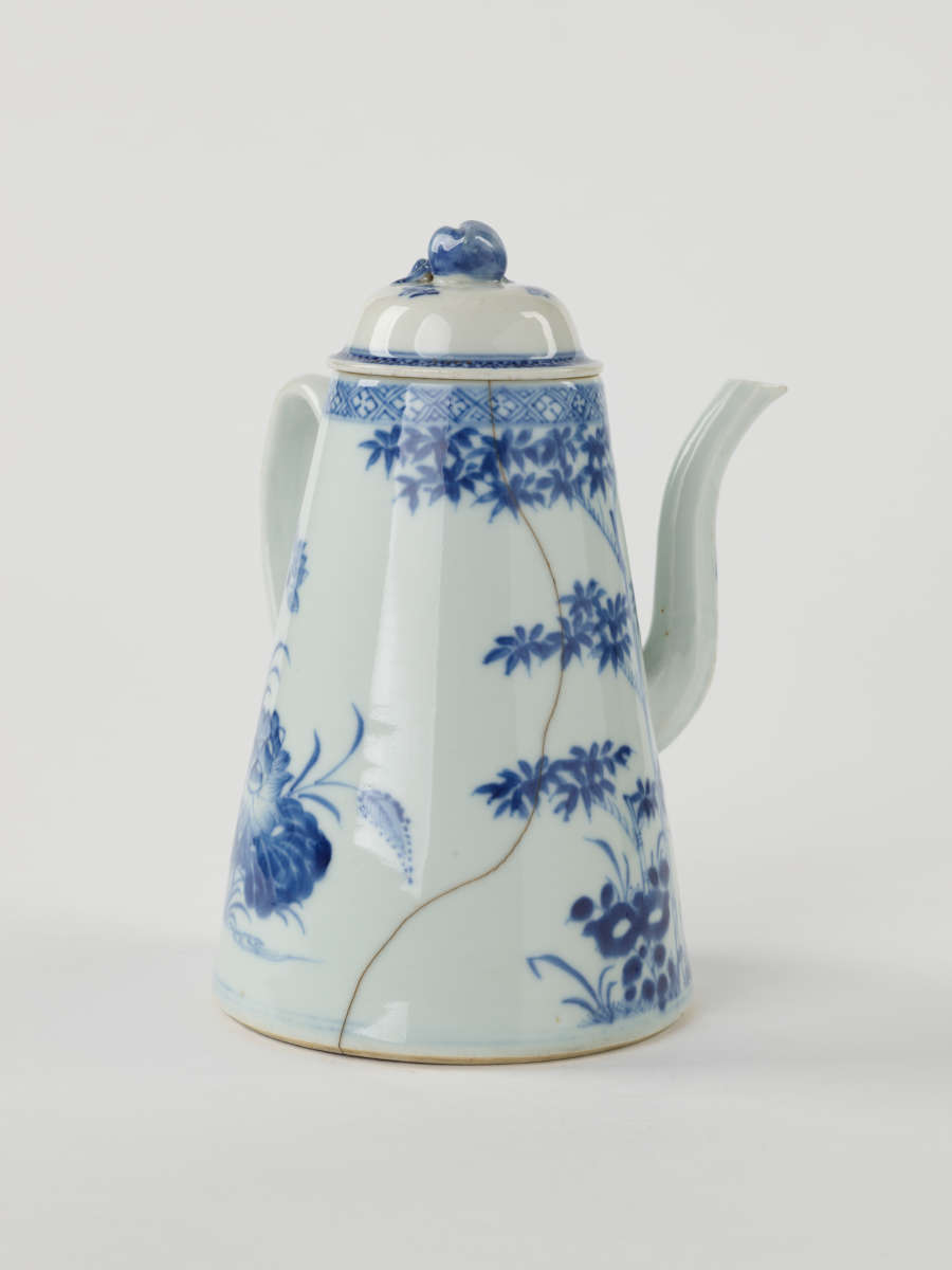 A white and blue teapot with floral decorations, a lid with a small semi spherical finial, spout, and a handle which is located approximately 90 degrees from the spout.