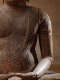 The torso and arm of a wooden Buddha with visible signs of wear and deep cracks against detailed carvings of a draped robe.