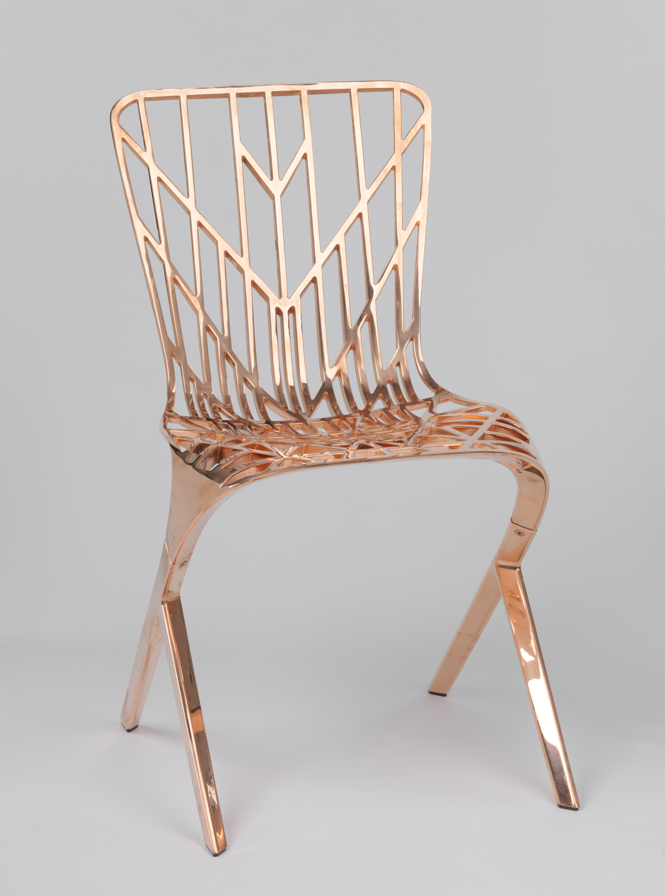 A copper-colored chair with an angular and open frame, with a symmetrical geometric pattern on the seat and backrest.