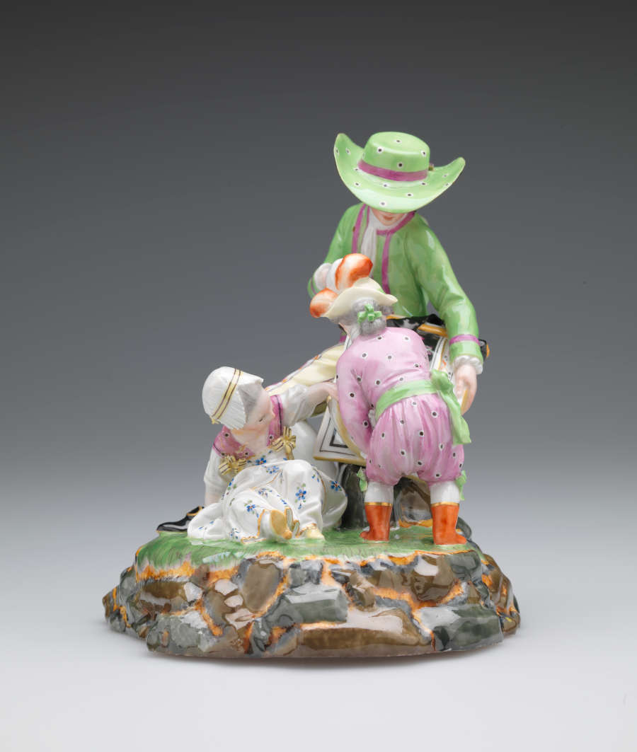 A sculpture with three figures in elaborate historical clothing. A seated light-skinned figure holds a roll of maps while one child examines. A second child sits near them.