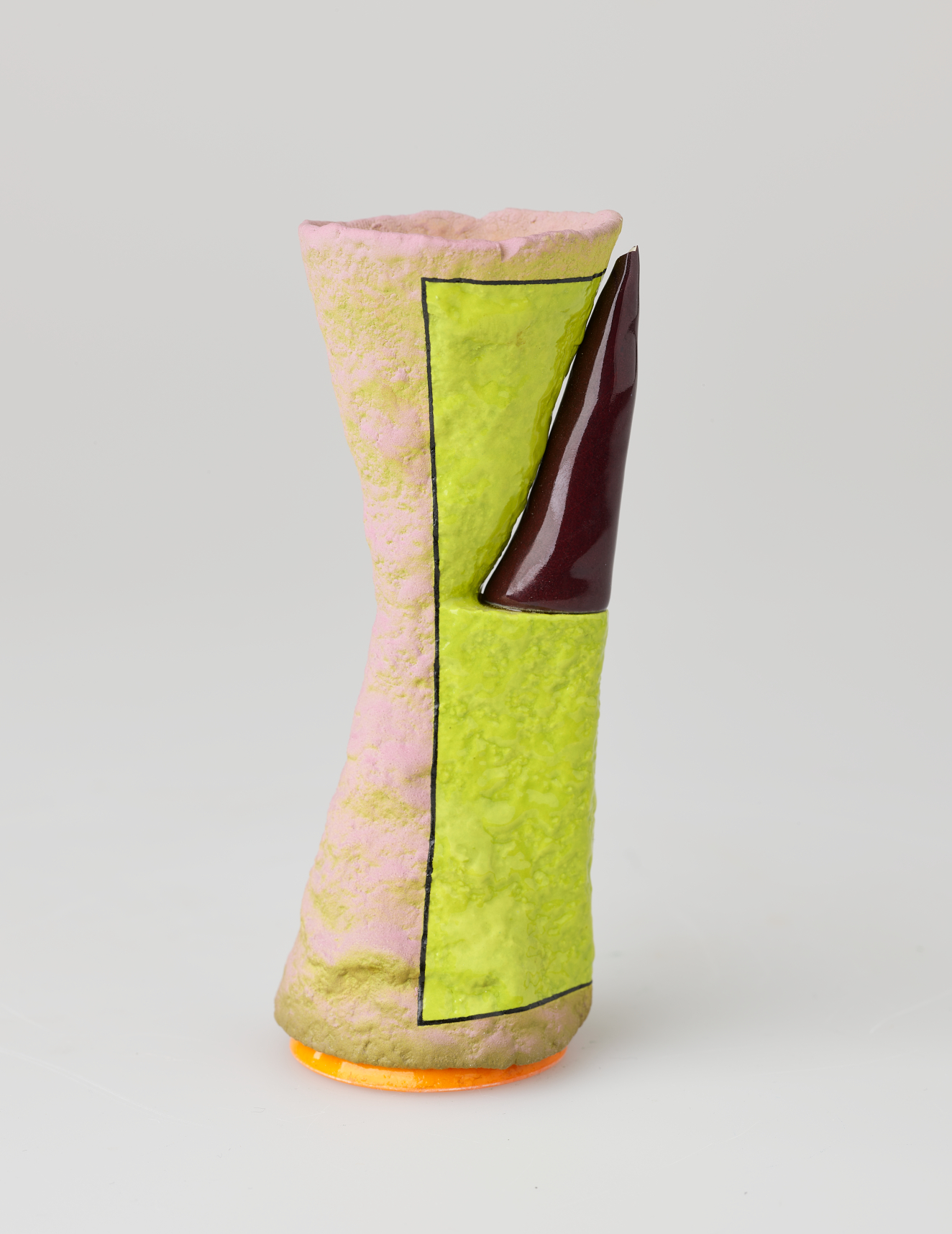 Textured ceramic vessel shaped like a soft hourglass in pale pink with a neon yellow pocket containing a glossy maroon triangle, all resting on a circular orange base.