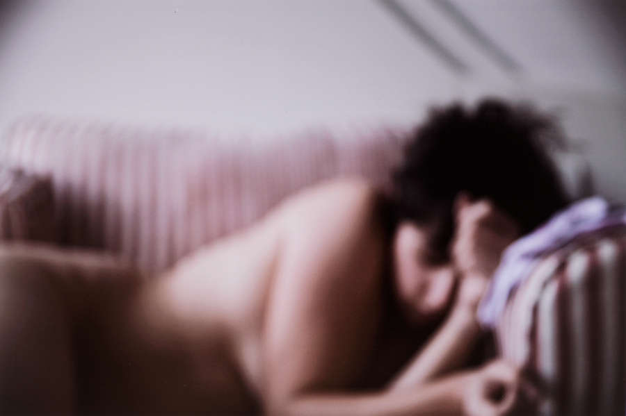 Blurry photo of a light-skinned woman from the waist up. She leans on her elbows and gazes down. 