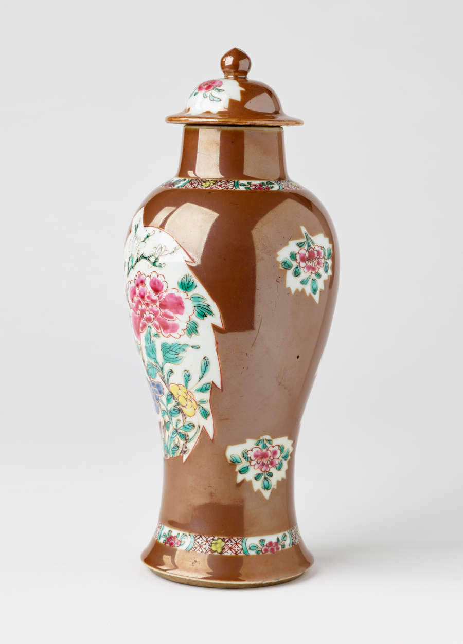 A brown and white covered vase with pink, green, blue, and yellow floral decorations.