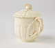  A cream-colored cup with a sculptural swirled handle, and lid with sculpted finial.