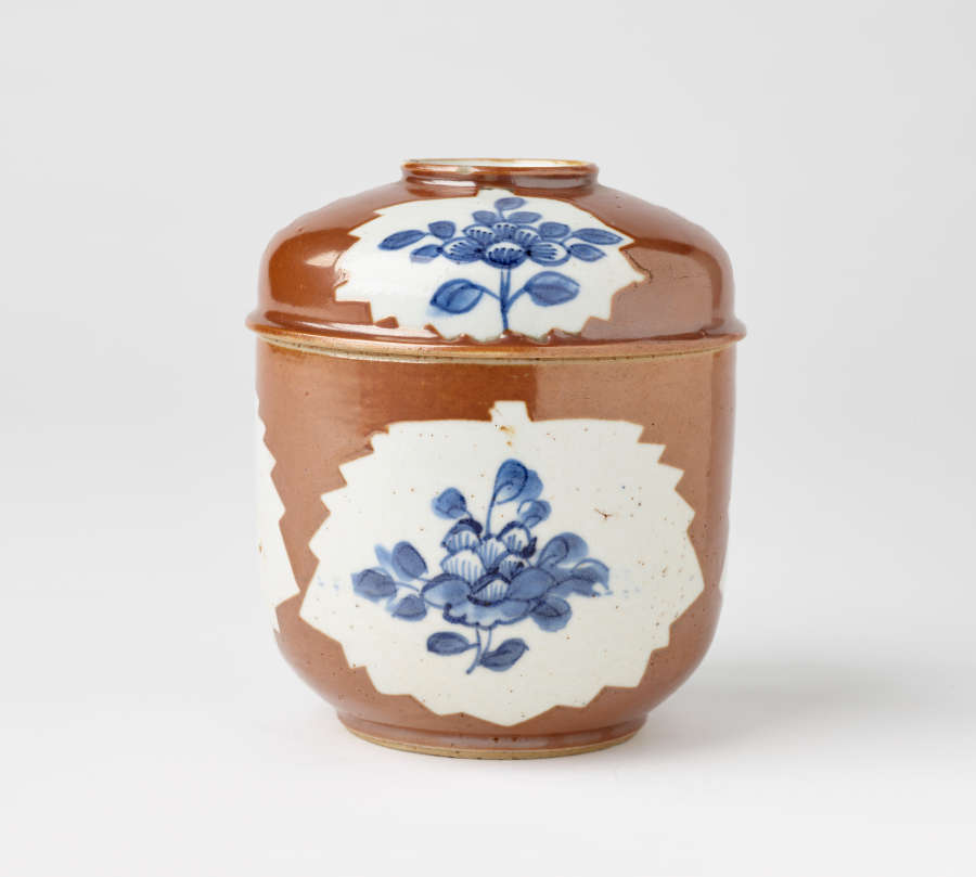 A brown covered bowl with blue floral decorations inside a white central ground.