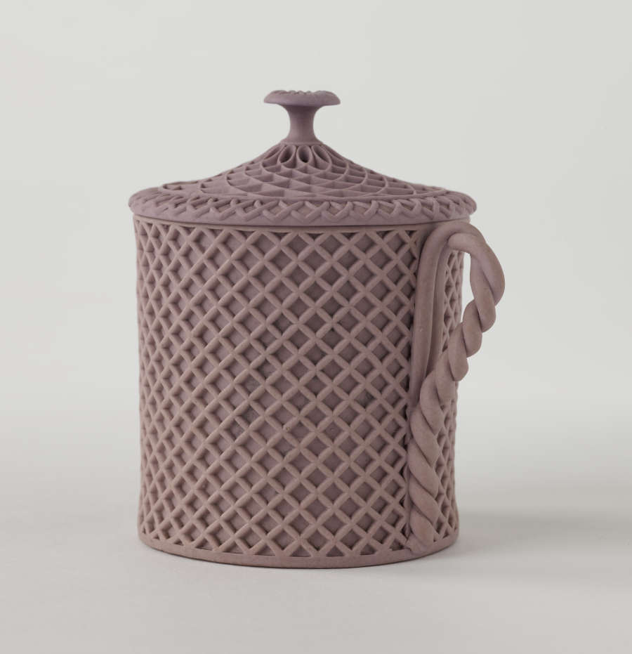 A purple covered cup with raised woven texture. The handle is sculptural and swirled.