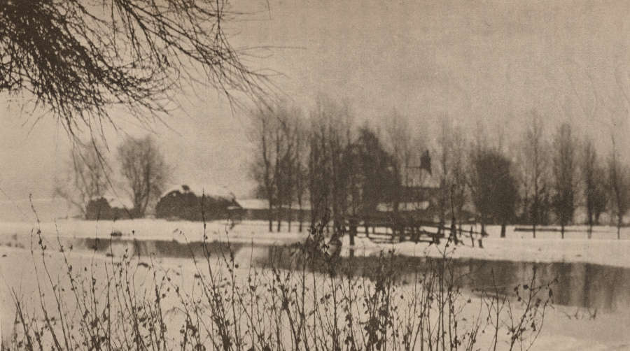 A black and white winter scene depicting farm houses surrounded by trees and a tranquil river, with bare branches and plants in the foreground.