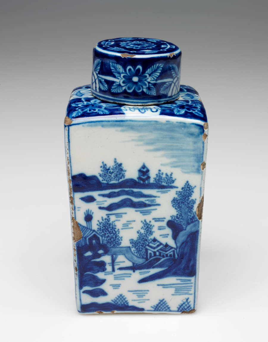 A rectangular vessel with blue and white architectural, landscape, and floral decorations. The lid is circular and with floral decorations.
