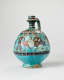 Bright turquoise jug with a spherical body and slender striped neck and handle. The jug’s body is decorated with illustrations of winged humanoid four-legged creatures and dark patterned stripes.