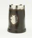 A brown tankard with silver band at top and a decorative silver crest.