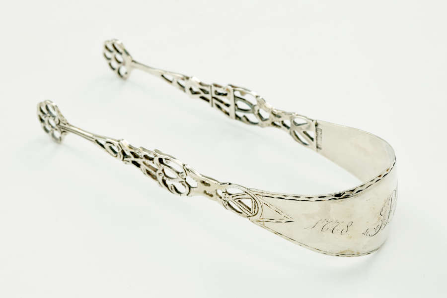 Silver sugar tongs with decorative cutouts.