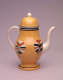 A yellow teapot with cream, orange, and brown circular designs dripping down at the bottom. Handle, spout, and final are cream colored.