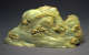 Pale green, smooth jade carving resembling mountain peaks dotted with clustered tree and a small waterfall in the center.  