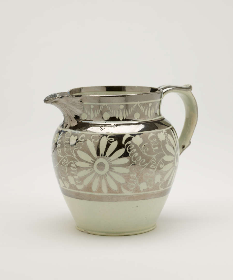 A silver-colored jug with floral motifs on the body of the vessel.