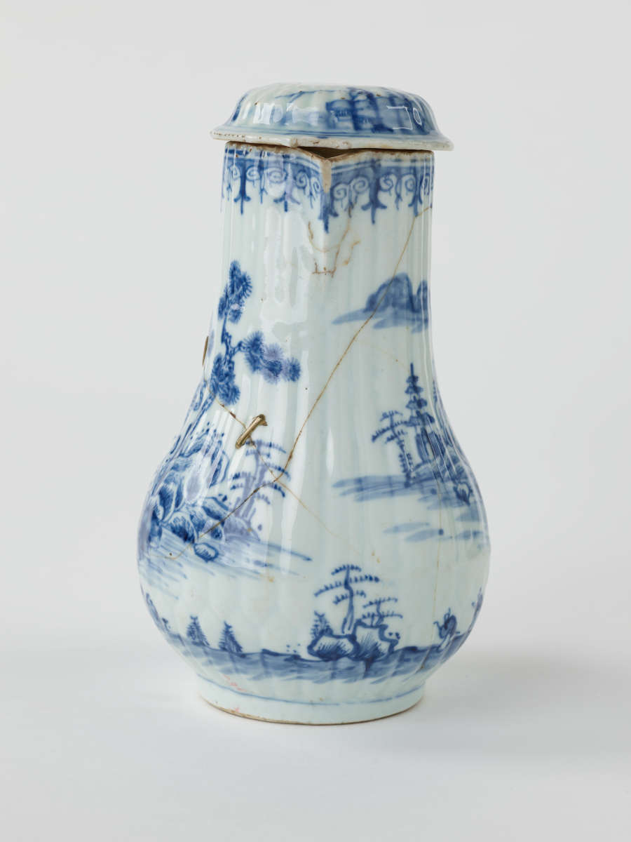 A white chocolate pot with blue decorations depicting floral and architectural elements.