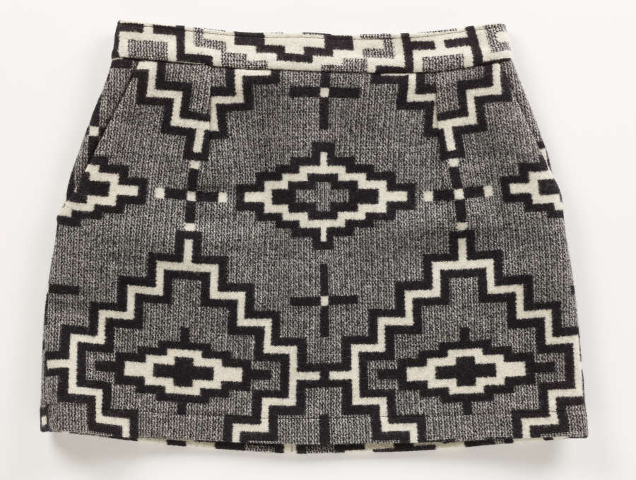 Back-view of a gray tweed skirt with black and white geometric diamond and cross motifs throughout. The top of the skirt is light gray with similar misaligned geometric patterns. 
