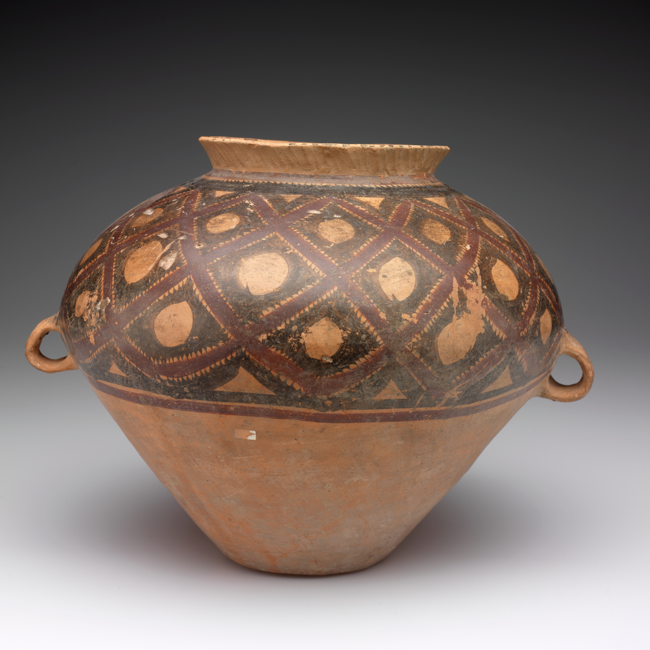 A large, rounded clay vessel with a narrow rim and two small handles,  decorated with red and black lattice.
