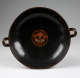 Top view of a cup with a wide mouth showing two handles peeking out from the edges. Its interior is glossy black with a terracotta illustration of an animal face.